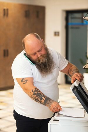 Bald bearded plus size man making copy on xerox