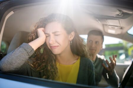 Upset turned away woman with closed eyes and a gesturing man, both in the car