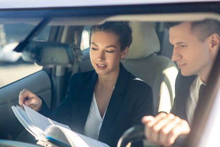 Good looking young woman showing documents to a man driving, they are attentive business partnersの写真素材