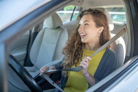 Smiling joyful young woman holding a safety belt while driving while sitting in a car