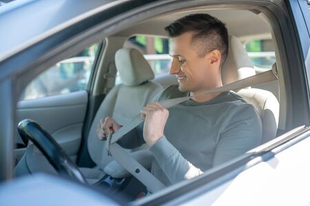 Interested man sitting in the drivers seat of a car, smiling with his seat belt on.