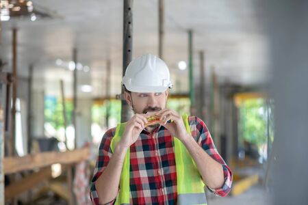 Building site. Building worker in yellow vest and helmet eating sandwichの写真素材