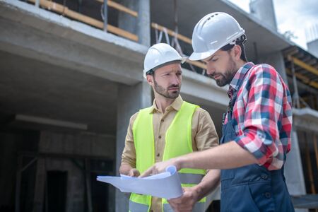 Building site. Building workers standing in front of crane, checking blueprint, brainstorming