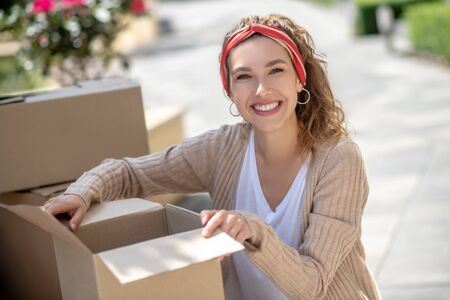 Packing. Pretty woman opening the cardboard and smiling widely