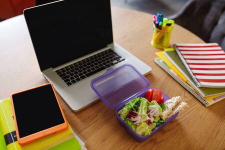 Lunchbox with snack. Purple open lunchbox with slices of vegetables and bread lying near the laptop.の写真素材