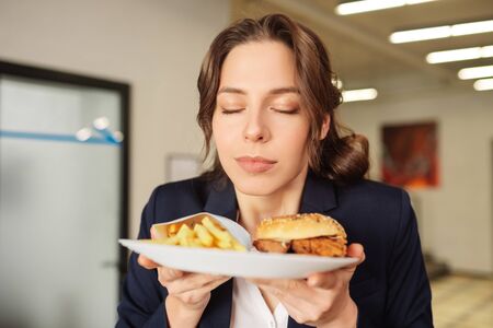 Favorite food. Contented face close-up girl holding a plate with fast food in front of her, happyの写真素材