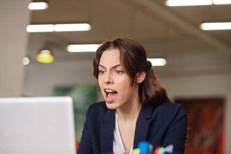Seriously and convincingly. Serious pretty young girl with open mouth sitting convincingly talking on a laptop in the officeの写真素材