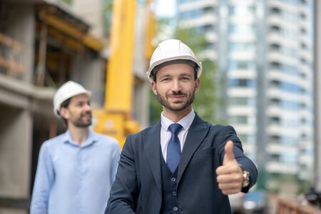Building site. Building supervisor showing thumb up, foreman standing behind him