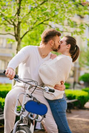 Love. Young kissing man on bicycle and woman standing nearby in park in great moodの写真素材