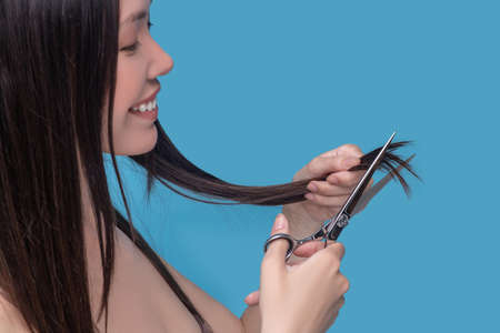 Getting rid of split-ends. A smiling long-haired woman cutting her split-ends with scissors.