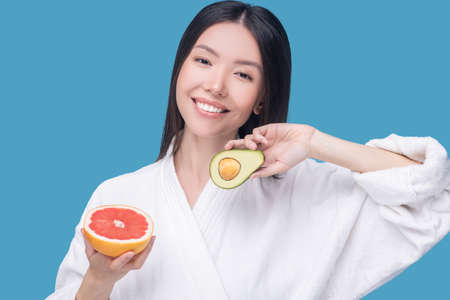 Vitamin containing products. A smiling woman holding an avocado and grapefruit