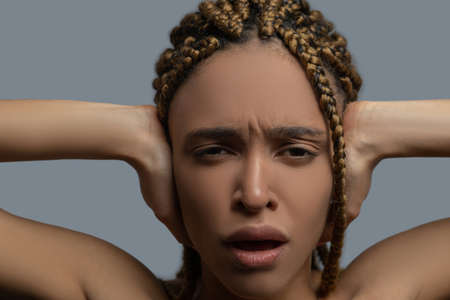 Inner pain. Frustrated young African American woman frowning, covering her ears with hands, screamingの写真素材