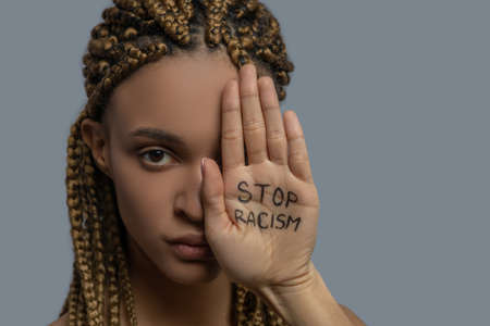Stop racism. Young African American woman covering half of her face with palm with stop racism letteringの写真素材