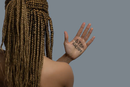 Stop racism. Young African American woman standing back to camera, showing palm with stop racism lettering above her shoulderの写真素材