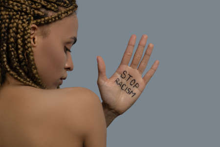Stop racism. Young African American woman standing back to camera, showing palm with stop racism...
