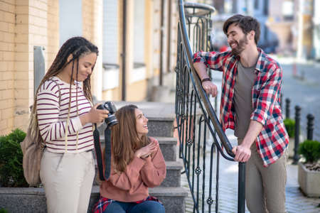 Rest while walking. Three friends resting during a walk around the city, near the stairs of the house, sunny dayの写真素材