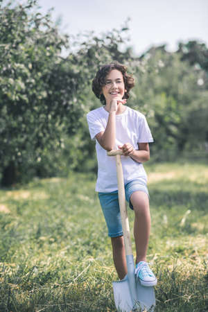 Gardener. Dark-haired boy standing with the spade in the garden and smilingの写真素材