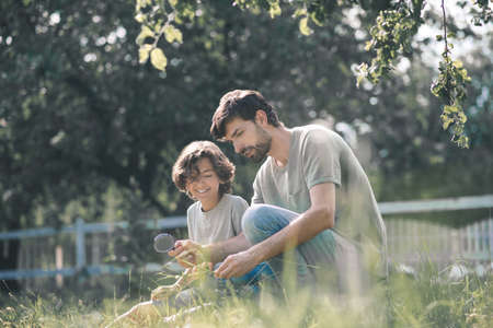 Nature lovers. Dark-haired boy and his father looking at the plant through magnifying glass and looking involvedの写真素材