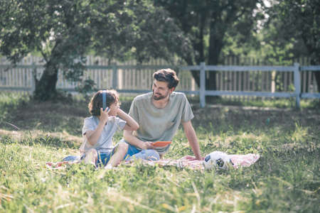 Resting together. A boy in earphones sitting near his dad and listening to musicの写真素材