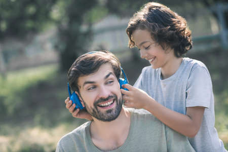 Earphones. Smiling son putting earphones on his fathers headの写真素材