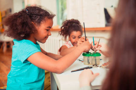 Painting in the class. A concentrated girl painting with a brush and watercolorsの写真素材