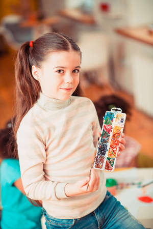 Young talents. A young girl holding a brush and a palette of watercolors