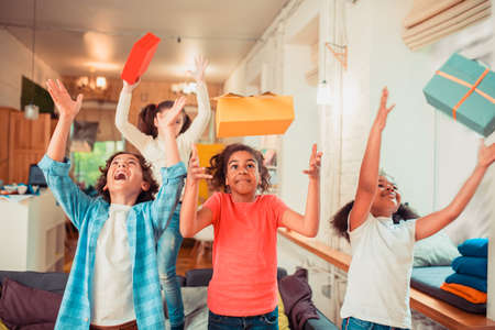Having fun together. Joyful and active kids throwing gift boxes