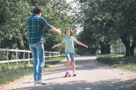 Happy family. Dark-haired boy riding a skateboard, his father feeling happyの写真素材