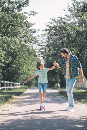 Learning to ride a skateboard. Cute boy riding a skateboard, his father holding his handの写真素材