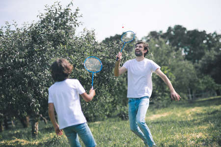 Badminton. Dark-haired boy and his father playing badminton and looking involvedの写真素材