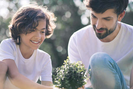 Small plant. Dark-haired boy and his dad looking at the plant and smilingの写真素材