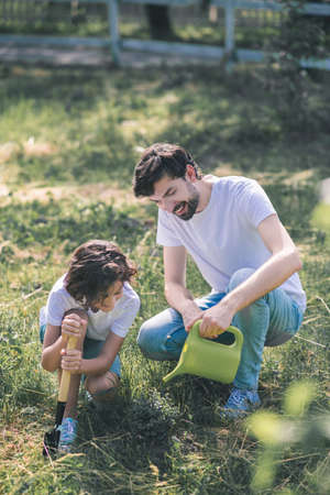 Watering. Dark-haired man watering the plant, his son watching himの写真素材