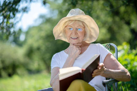 Reading outdoor. An excited elderly woman reading an interesting book