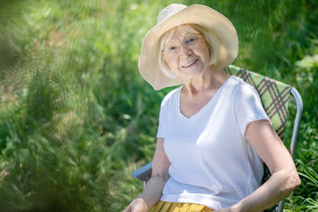 Outdoor. An elderly woman wearing a hat sitting in the gardenの写真素材