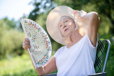 Elegant woman. A woman relaxing in a deck chair with a fanの写真素材