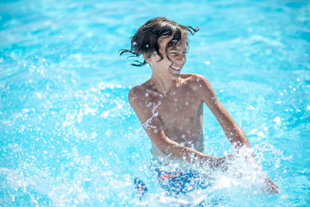 Splashes, fun. Energetic dark-haired boy standing in water with drooping eyelids making splashes by...