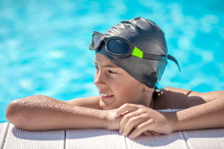 Interesting there. Boy in wet swimming cap resting his hands on edge of pool looking with his head turned to sideの写真素材