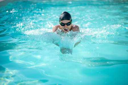 Swimmer in water. Swimmer in black swimming cap and goggles with his mouth open in water correctly moving forwardの写真素材