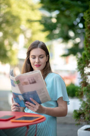 Pleasant time. Charming brown-haired female reading sitting in cafe, reading newspaperの写真素材