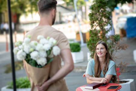 Lovey date. Young male standing in front of smiling female, hiding flowers behind his backの写真素材