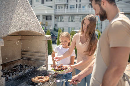 Grilling. Dad grilling meat while his daughter and wife watchingの写真素材
