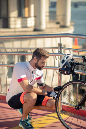 Bicycle, wheel. Serious cyclist in sportswear crouched near wheel of his bike on the street on sunny dayの写真素材