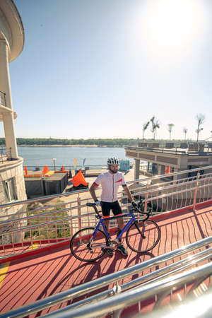 New impressions. Bearded man in a sports helmet and clothes standing with bicycle on the bridge, in good moodの写真素材