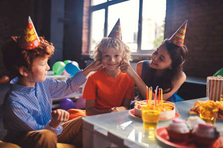 Two friends pulling cheeks of their friend and smilingの写真素材