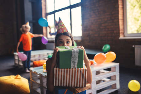 Cute girl in a hat holding presents and feeling amazedの写真素材