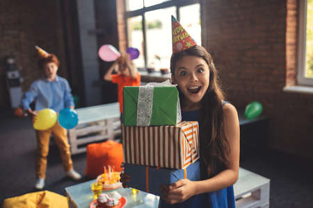 Pretty girl in a hat holding presents and looking excitedの写真素材