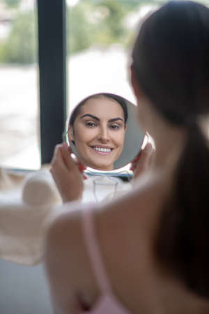 Love myself. Cute woman in pink lingerie feeling good looking at herselfの写真素材