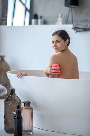 In the bathroom. Woman holding a red sponge and feeling pleasedの写真素材