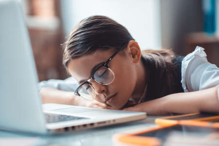 Tired. Surprised brunette girl in eyeglasses napping at the laptop