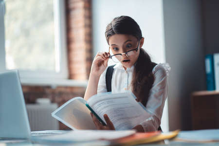 Shocked. Brunette girl in eyeglasses reading a report and looking shockedの写真素材